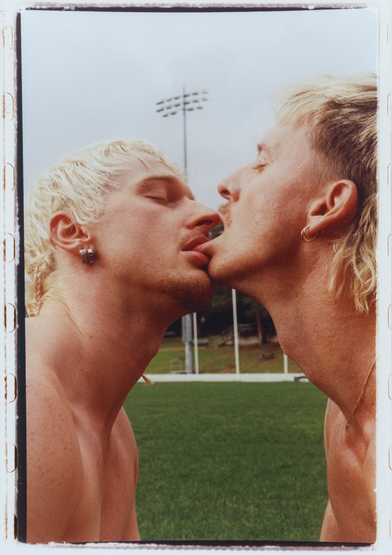 Two men leaning towards a kiss on a football field, within a photographic border.