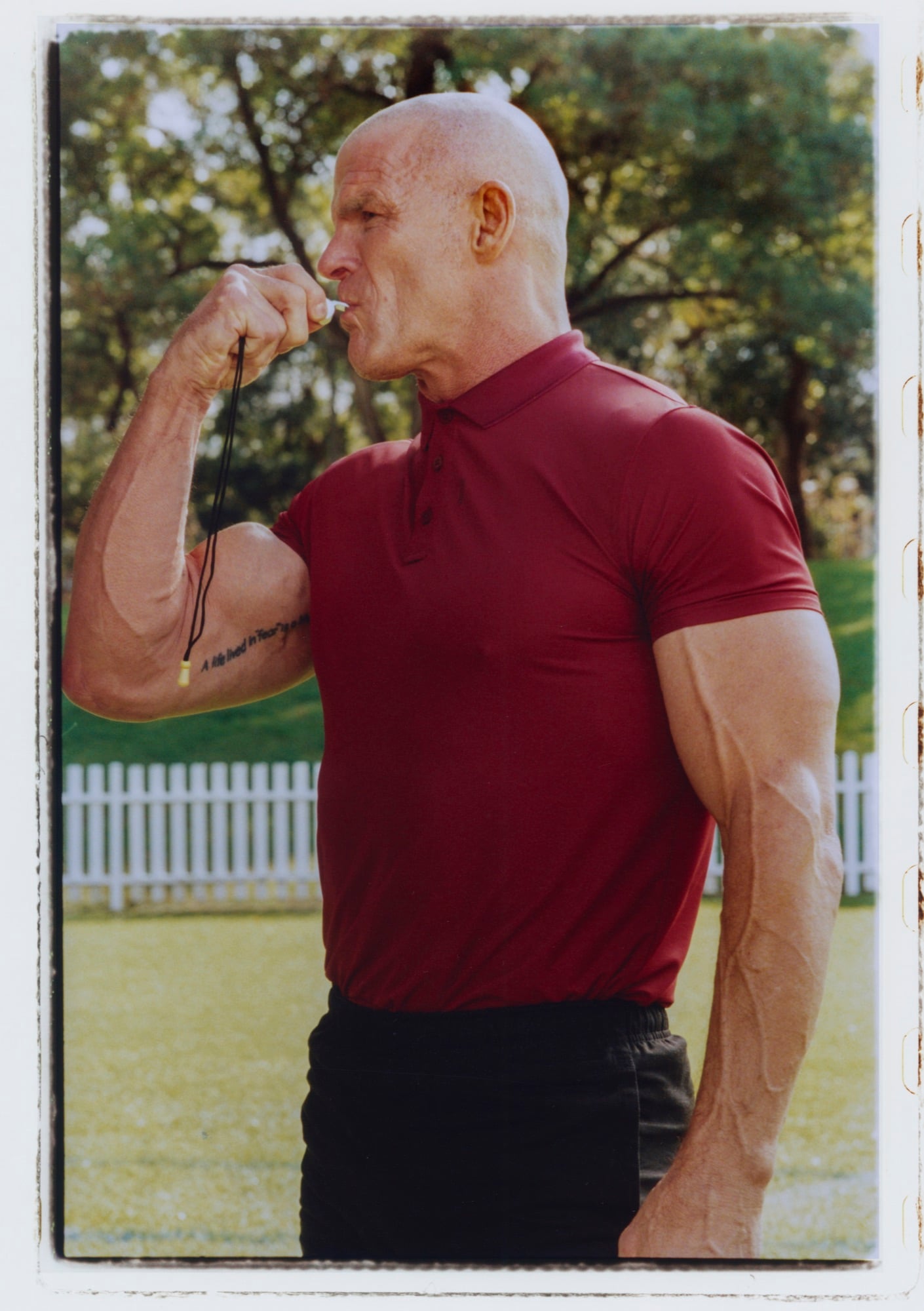 A man in a red polo shirt holding a whistle, within a photographic border.