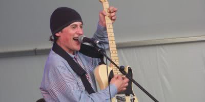 Lead singer of Television Personalities, Dan Treacy live on-stage singing into a microphone and strumming a guitar