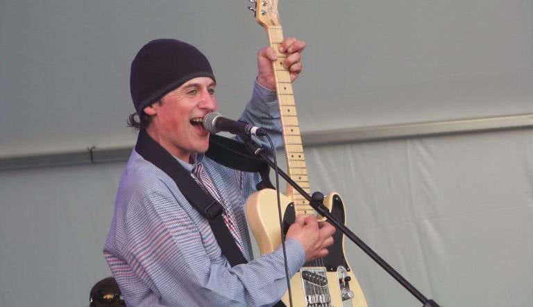 Lead singer of Television Personalities, Dan Treacy live on-stage singing into a microphone and strumming a guitar