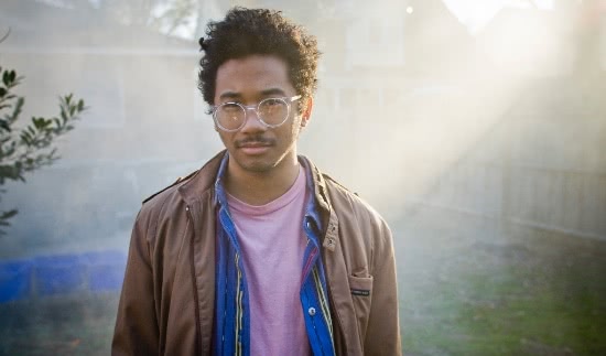 Toro Y Moi standing in a hazy suburban landscape