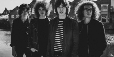 The four members of British rock band Catfish And The Bottlemen standing next to a river.