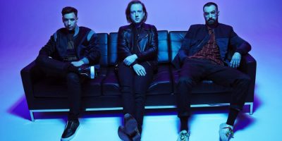 The members of Two Door Cinema Club, seated in what is presumably a Drake music video.