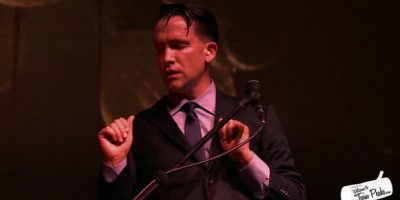 Jamie Stewart of Xiu Xiu, wearing a suit and standing with eyes closed behind a keyboard and microphone.