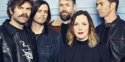 The members of Slowdive standing in front of a blue wall