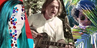 Girls with blue hair and diamonties on her face, man in white shirt playing guitar, man in blue had standing behind leaves