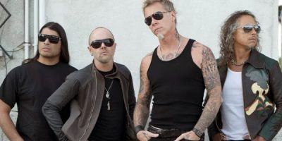 Metallica band members standing in front of a white wall wearing black clothing and sunglasses