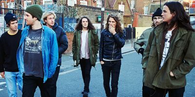 seven men walking in the street wearing jeans, jackets and beanies.