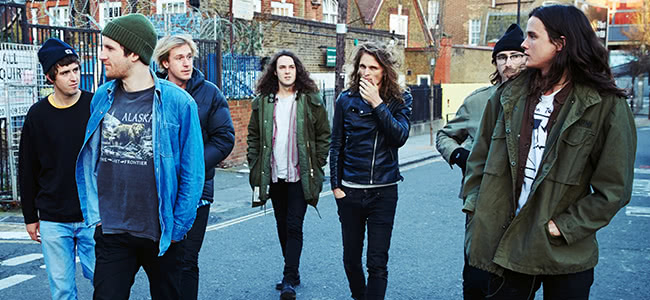 seven men walking in the street wearing jeans, jackets and beanies.