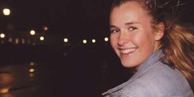 Girl with blond hair looking back at camera wearing a denim jacket at night time