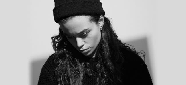 Tash Sultana looking down in black top and black beanie.