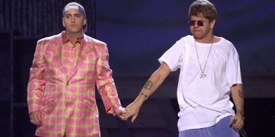 Eminem wearing a pink and green spotted suit holding hands with Elton John who is wearing a white tshit and blue tracksuit pants