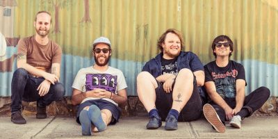 Smith Street Band sitting on the cement in front of a tin wall