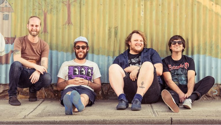 Smith Street Band sitting on the cement in front of a tin wall