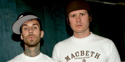 Tom DeLonge and Travis Barker looking at camera wearing white tshirts and black caps