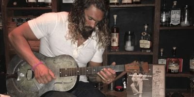 US actor Jason Momoa playing a guitar owned by C.W. Stoneking