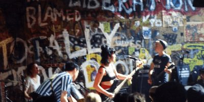 Bikini Kill play live against a wall of graffiti