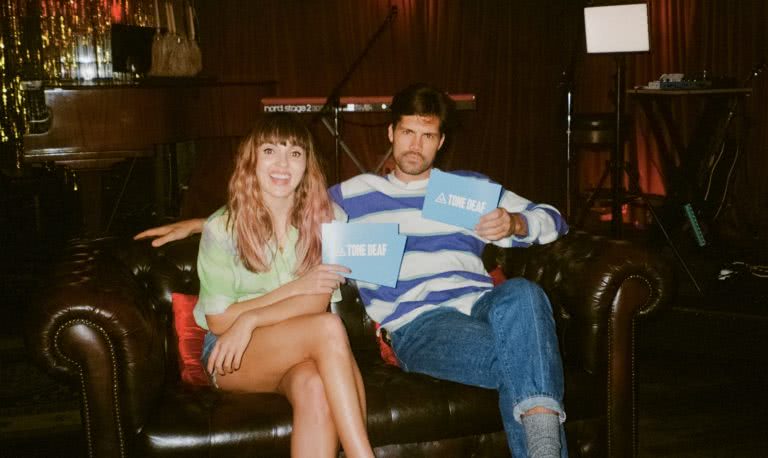 Josephine and Anthony sit on couch about to play 'Who's Most Likely To?' Game