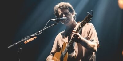 Bernard Fanning singing into a microphone with a guitar in his hands