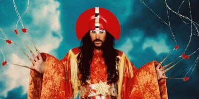 Luke Steele of Empire of the Sun wearing an ornate red and gold costume against a blue background