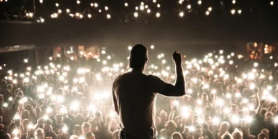 360 seen from behind with one arm raised, facing a crowd illuminated by phone lights.