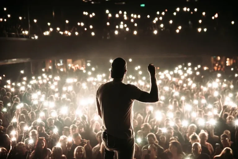 360 seen from behind with one arm raised, facing a crowd illuminated by phone lights.