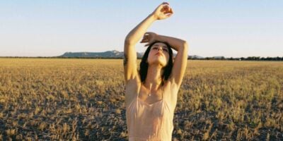 Grace Cummings standing in a golden field with her arms raised above her head.