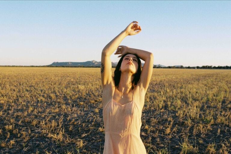 Grace Cummings standing in a golden field with her arms raised above her head.