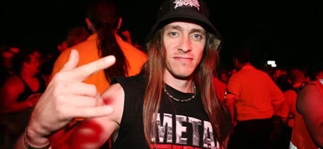 Man standing close to camera, with his fingers pointing up in a black singlet and black hat