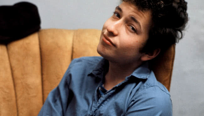 Man sitting on a lounge wearing a blue shirt smiling at the camera